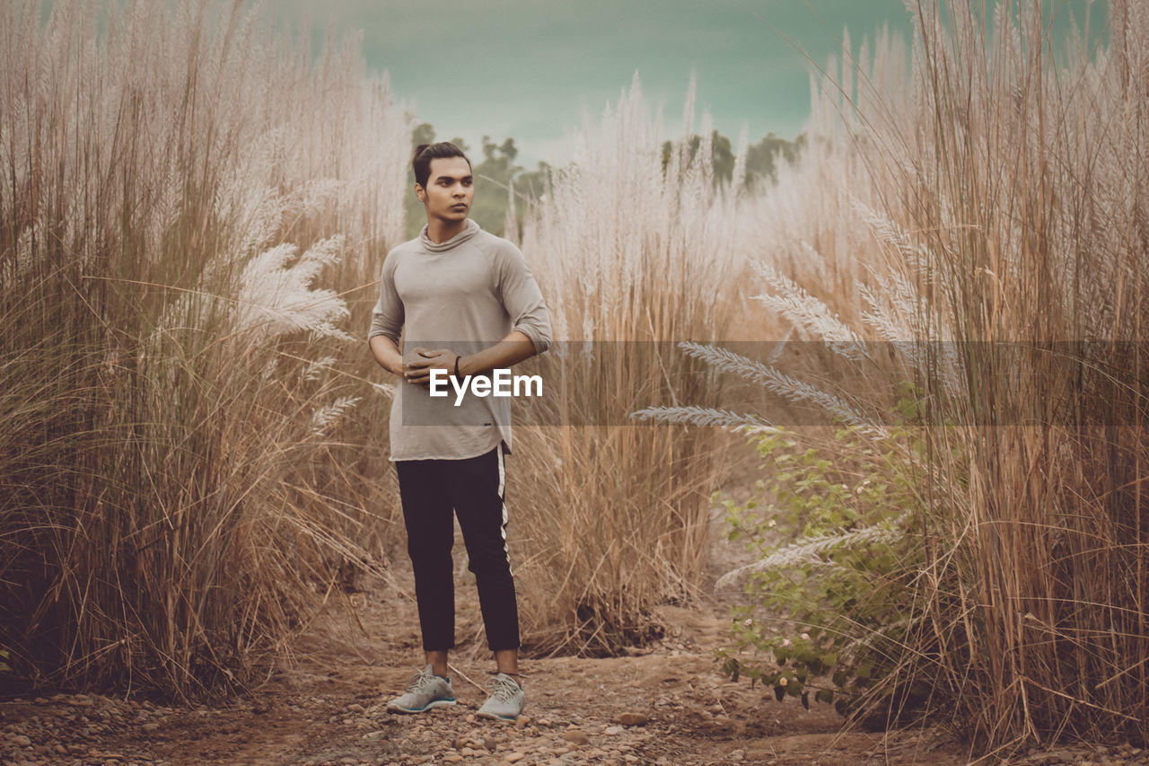 Full length of young man looking away while standing on field