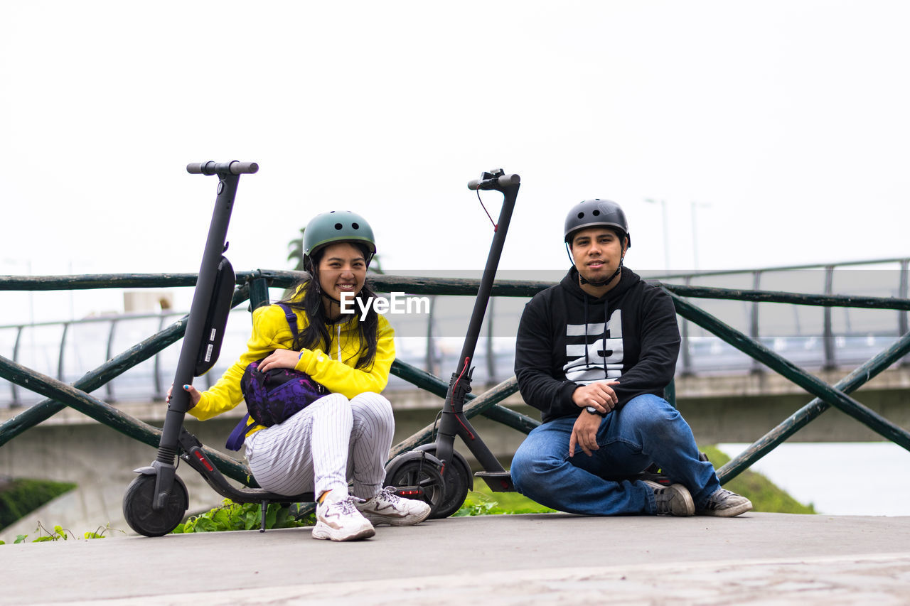 Portrait of smiling coupe sitting on push scooter against clear sky