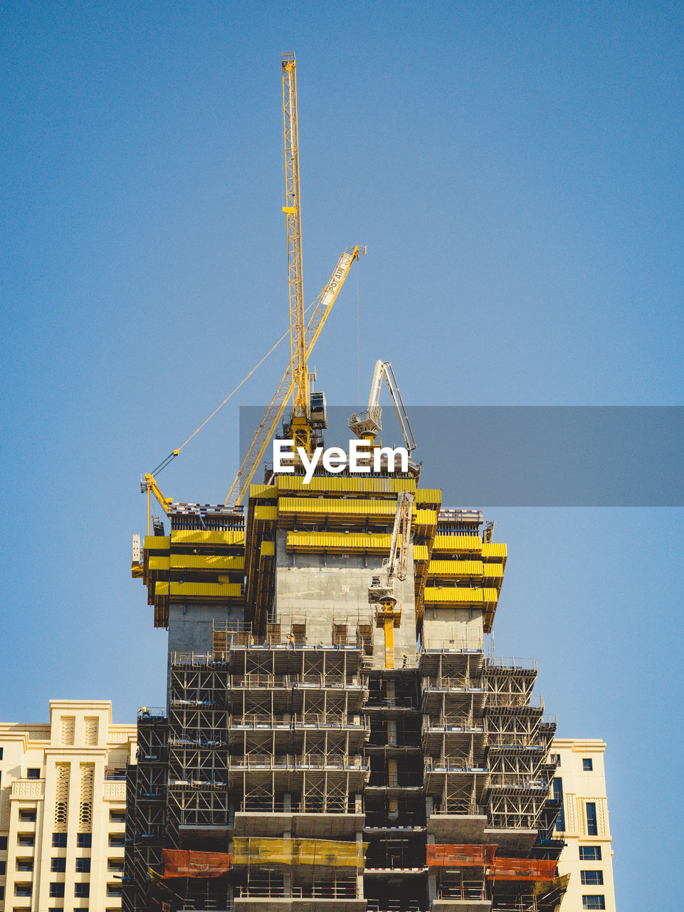 Low angle view of crane by building against clear blue sky