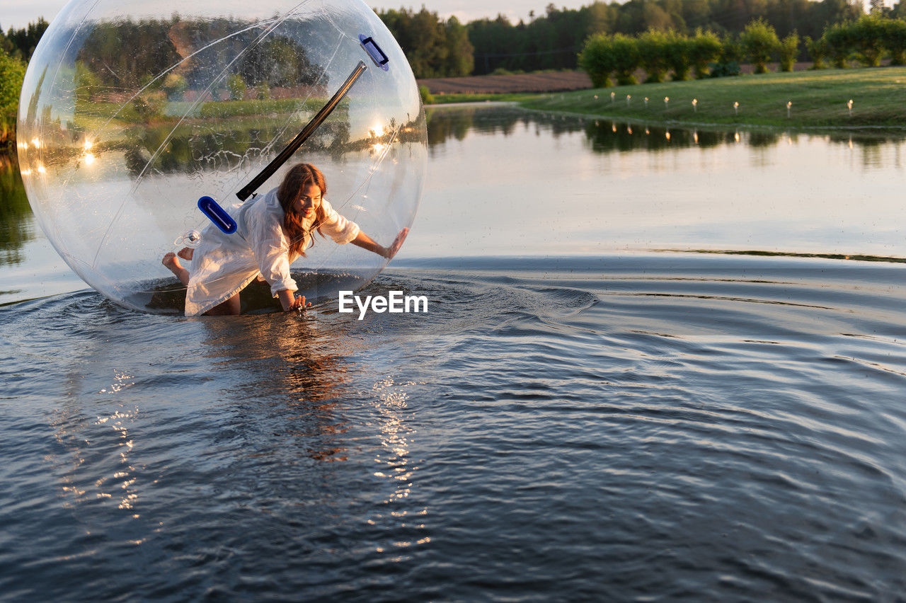 Water ball similar to zorb or human hamster ball with young woman inside on pond surface