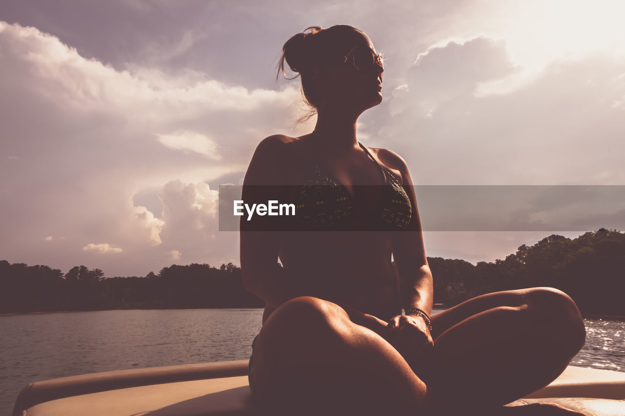 Woman sitting on boat in sea against sky during sunset