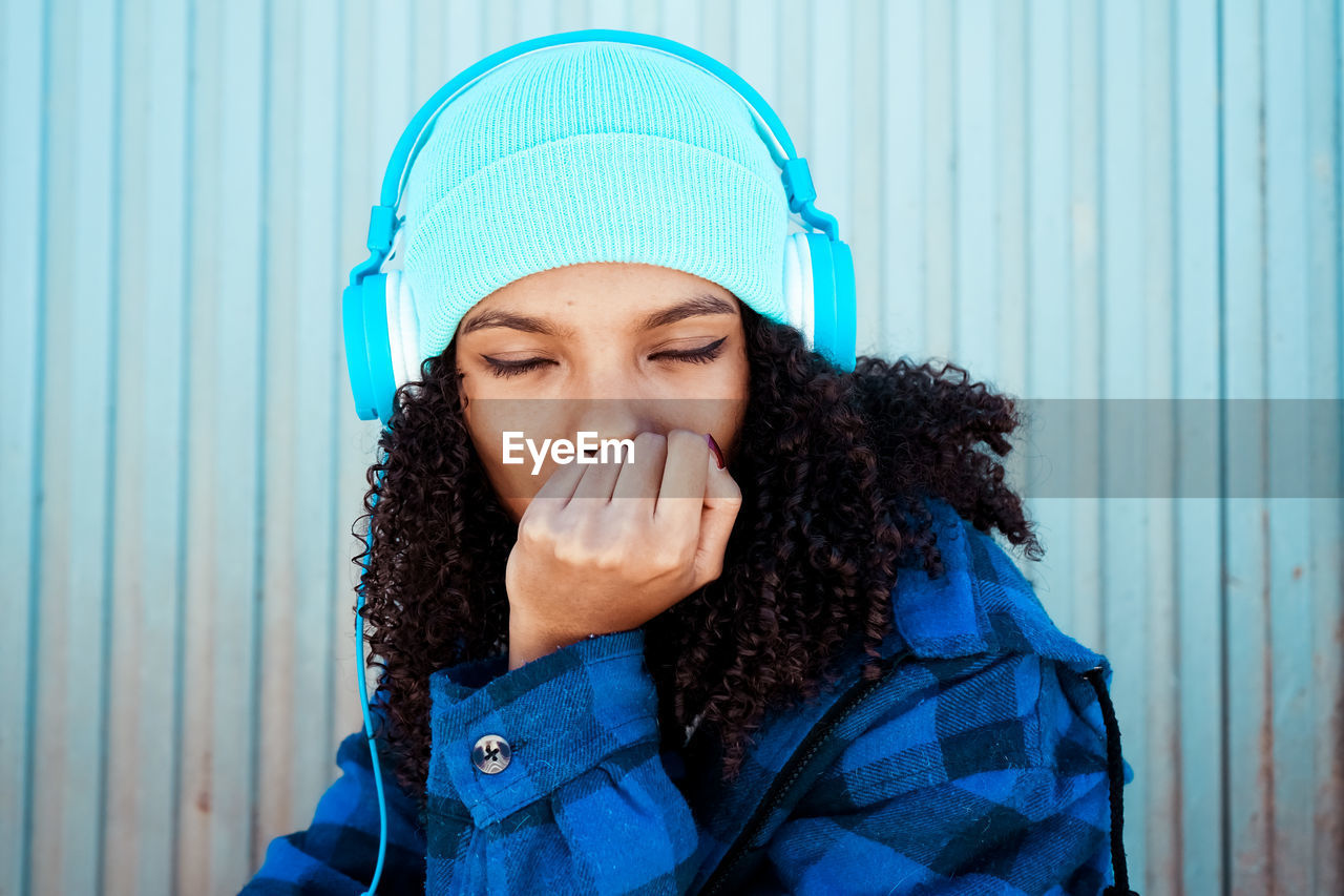 Young woman listening to music on headphones against closed shutter