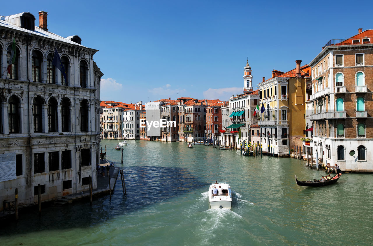 Gondolas moving on grand canal amidst buildings against clear blue sky