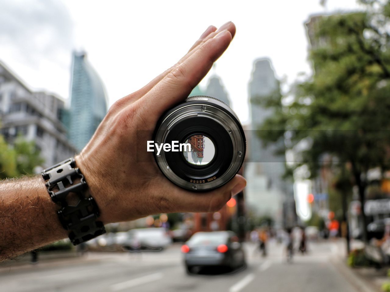 Cropped image of hand holding lens on city street