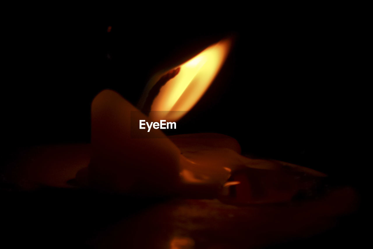 CLOSE-UP OF BURNING CANDLE IN DARKROOM