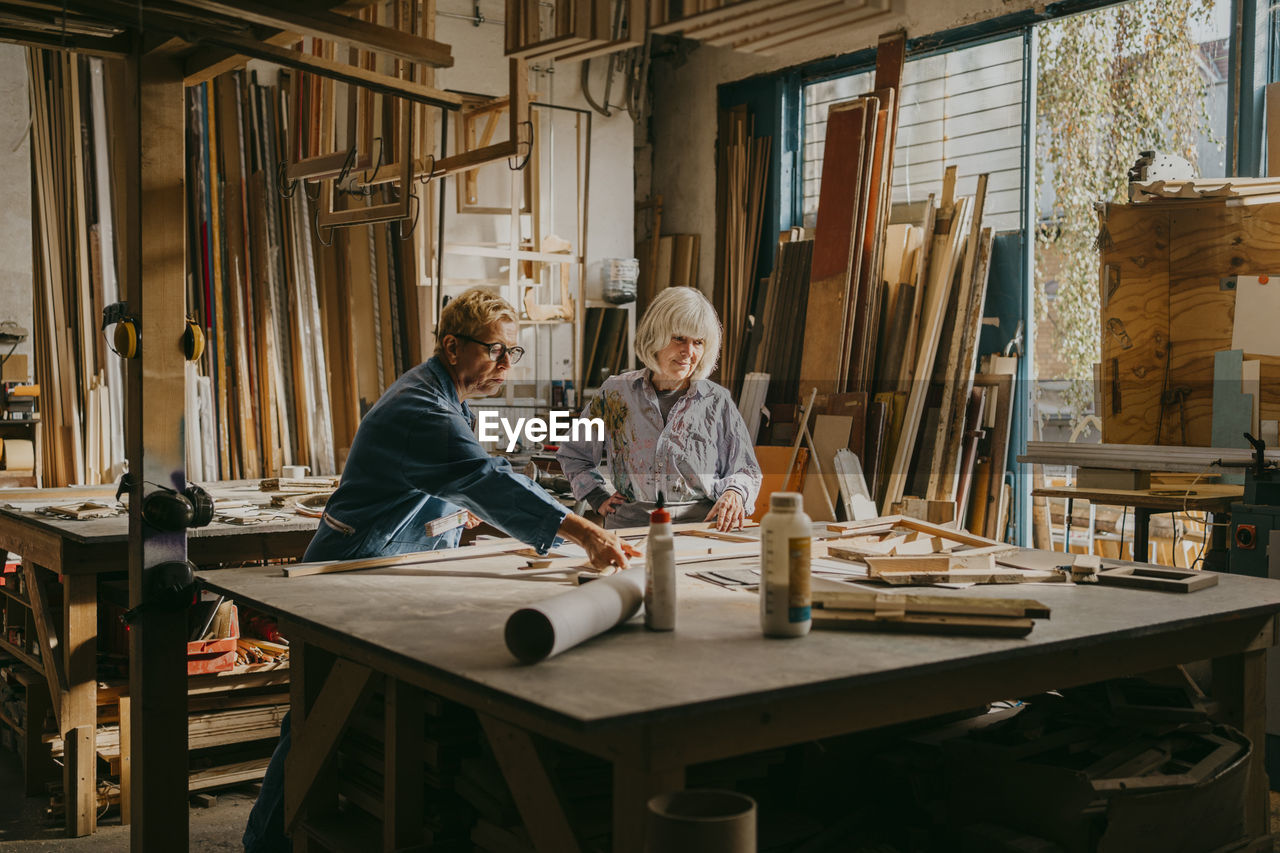 Senior female carpenter assisting colleague while working at repair shop