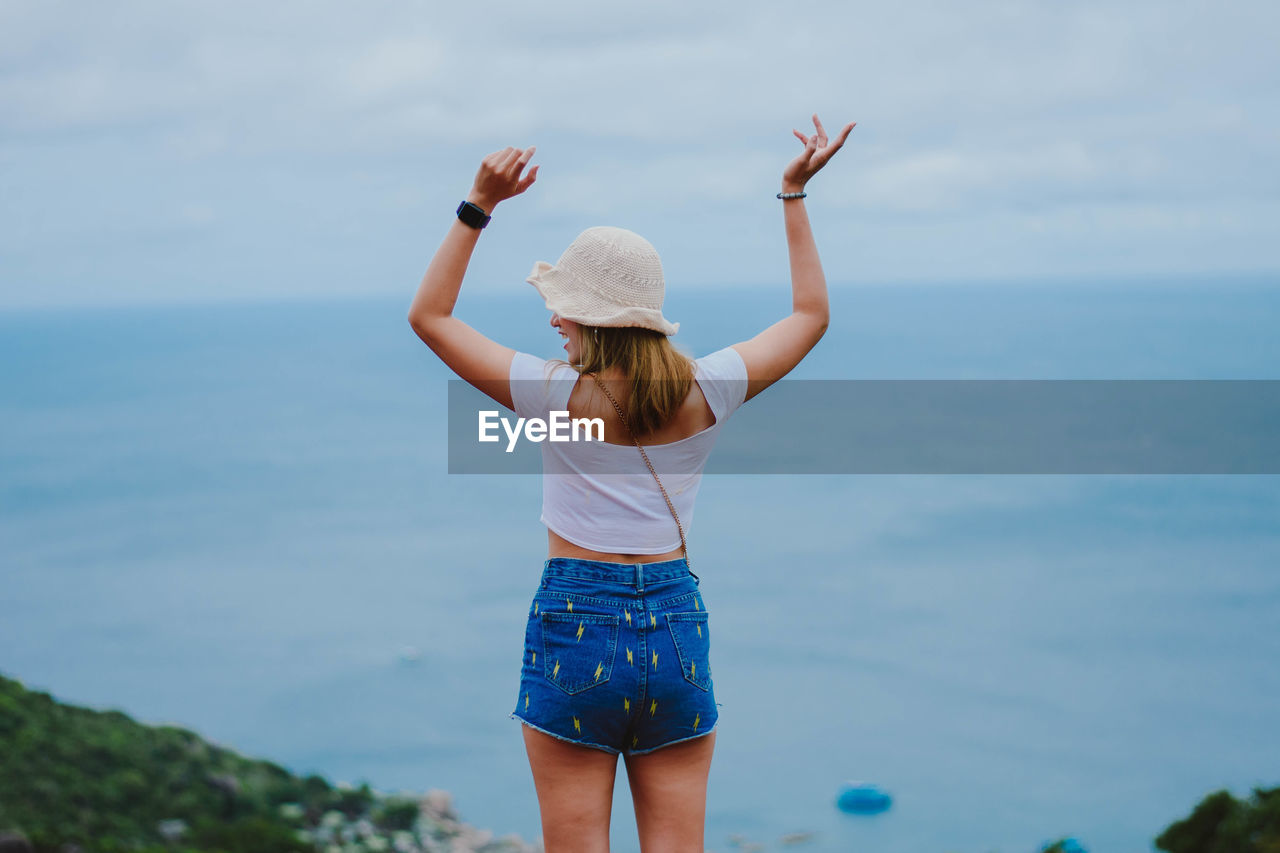 FULL LENGTH REAR VIEW OF WOMAN STANDING IN SEA AGAINST SKY