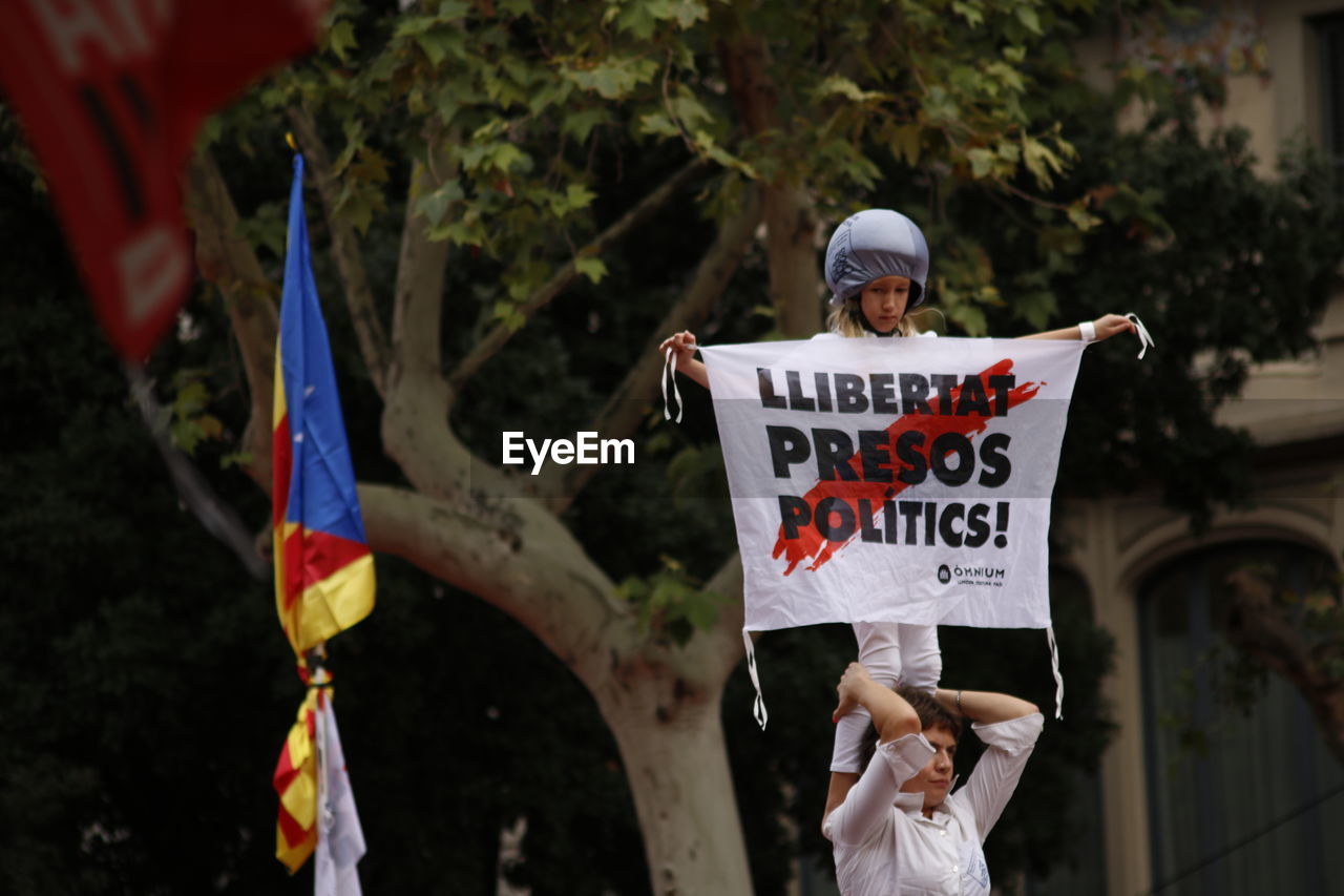 REAR VIEW OF PEOPLE HOLDING FLAG AGAINST TREE