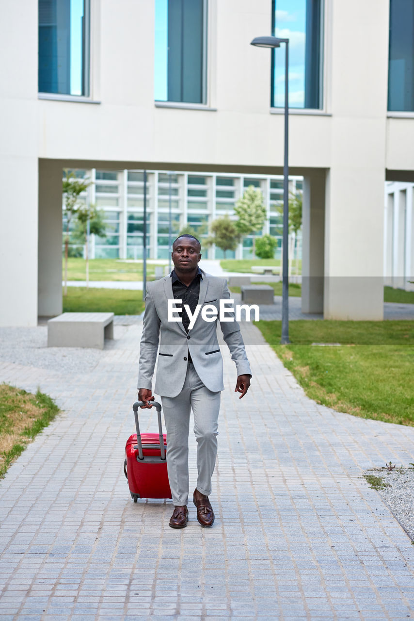 African-american in a white suit and a red suitcase.