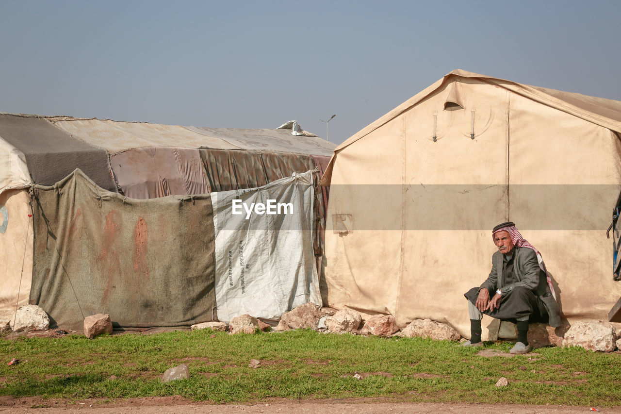 one person, adult, tent, men, architecture, clothing, nature, full length, sky, rural area, built structure, lifestyles, copy space, building, building exterior, occupation, day, landscape, outdoors, house, rural scene, hut, poverty