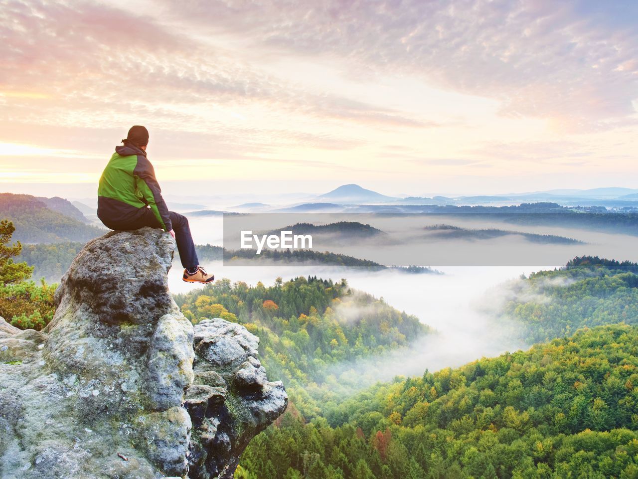 Hiker man take a rest on mountain peak. man sit on sharp summit and enjoy spectacular view.