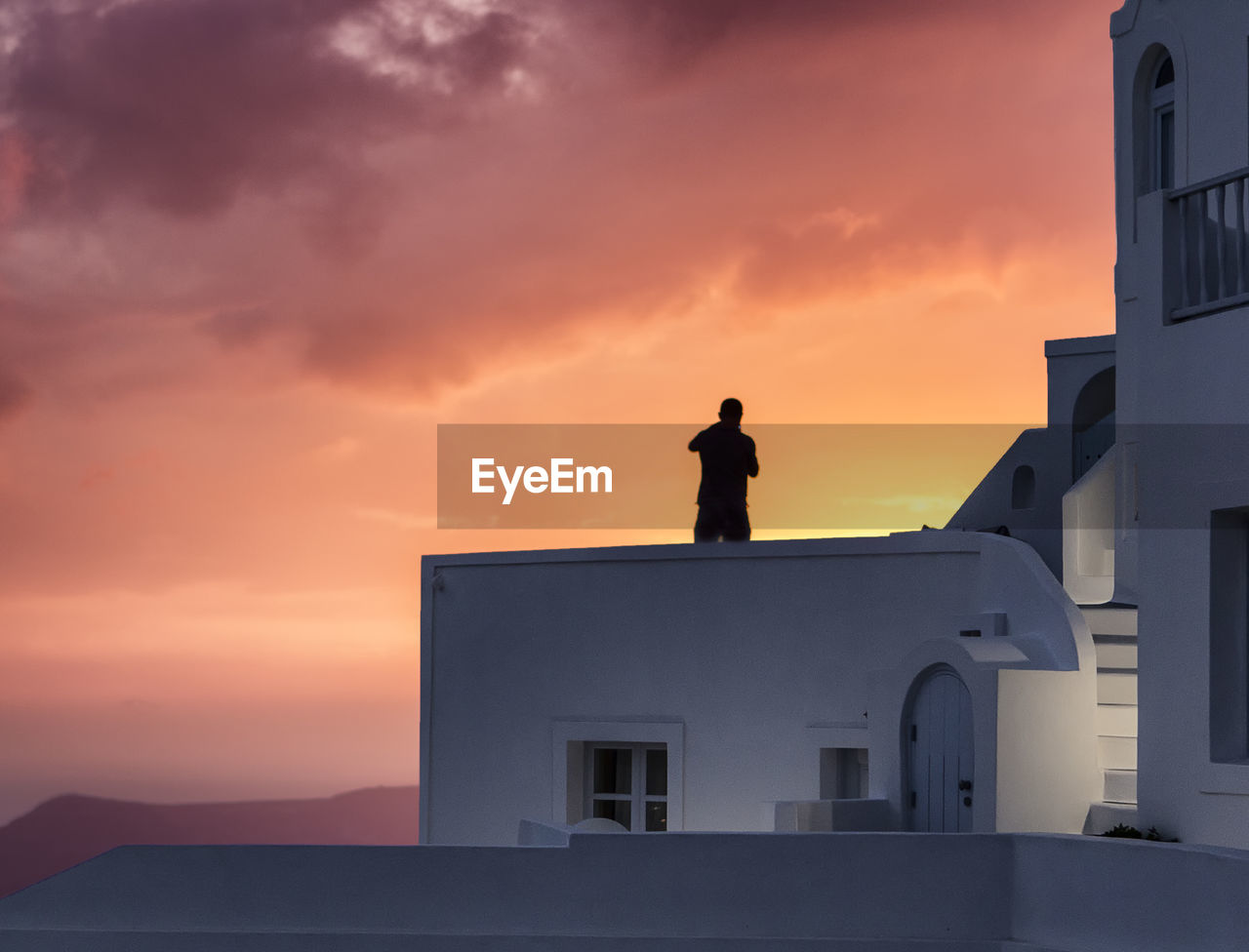 Silhouette man standing on building against sky during sunset