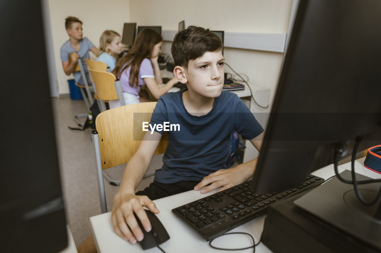 Boy surfing internet on computer while sitting on chair in classroom at school
