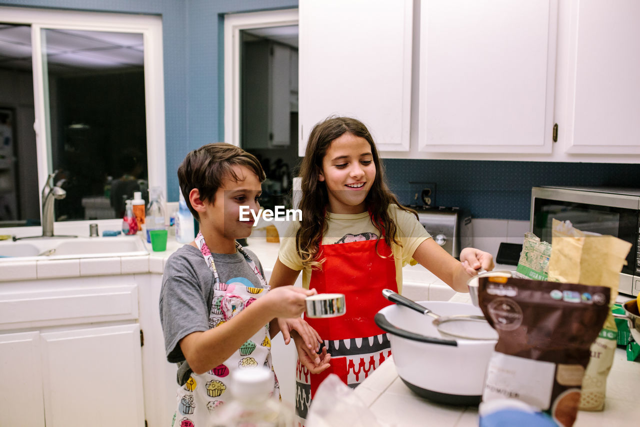 Brother and sister smile while baking in the kitchen at night