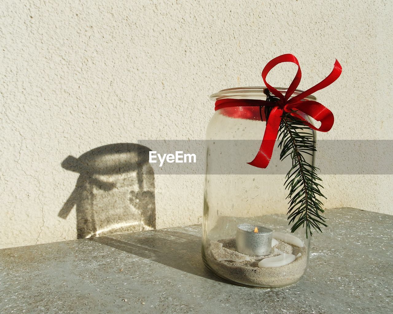 Close-up of red ribbon tied on glass jar against wall