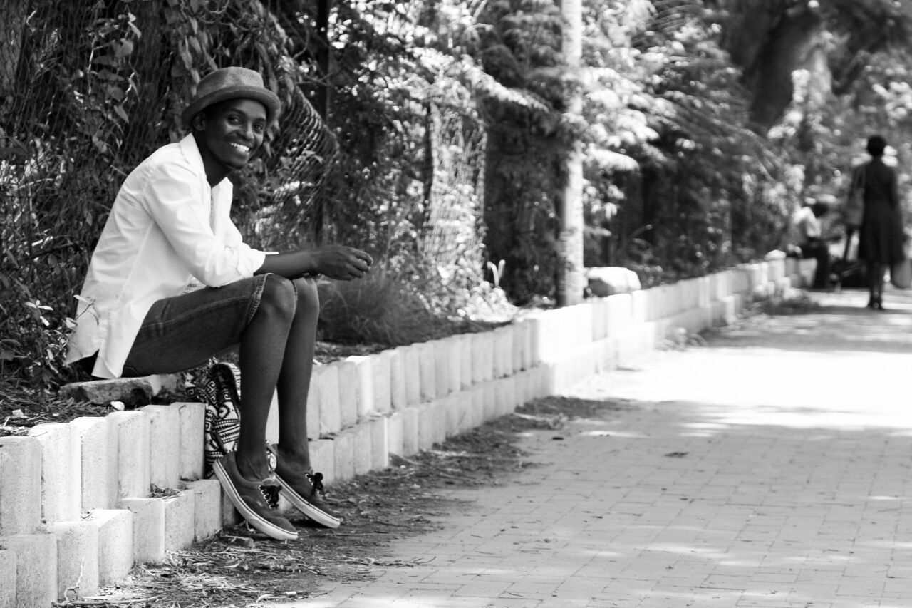 Smiling man sitting on retaining wall by trees at park