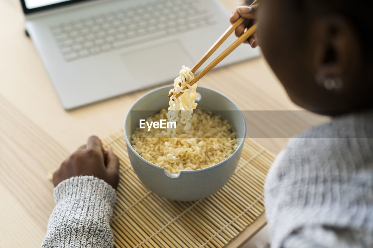 Young woman holding noddles in chopsticks while sitting at home