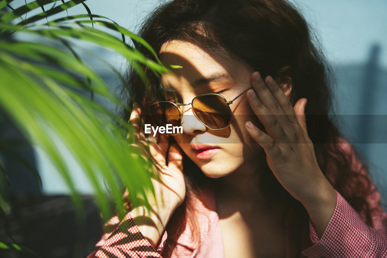 Close-up of woman wearing sunglasses sitting by plants