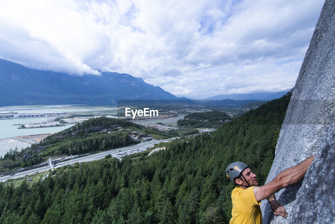 Man blurry foreground climbing with squamish city forest background
