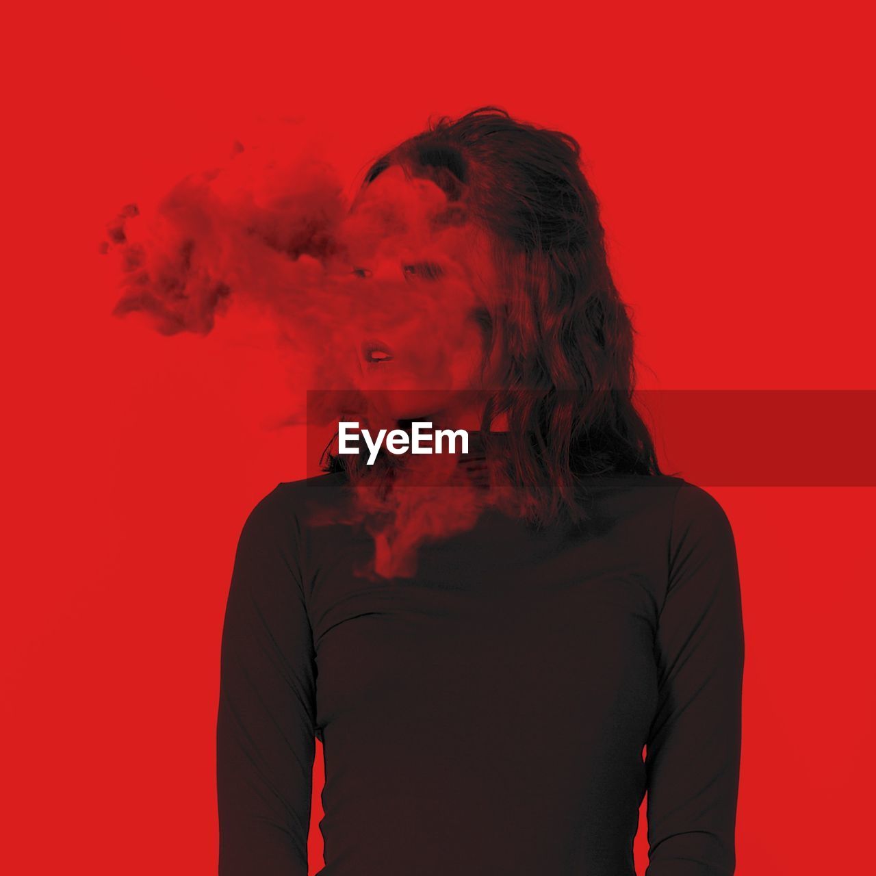 Young woman with smoke standing against red background