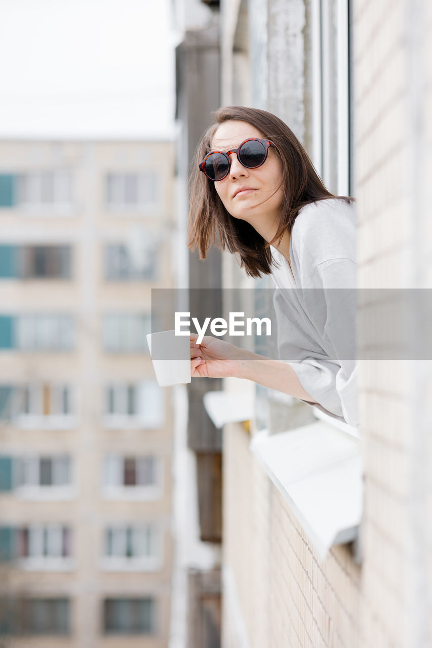 Young woman wearing sunglasses standing against built structure