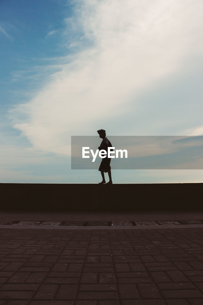 Man walking on wall by sidewalk against sky