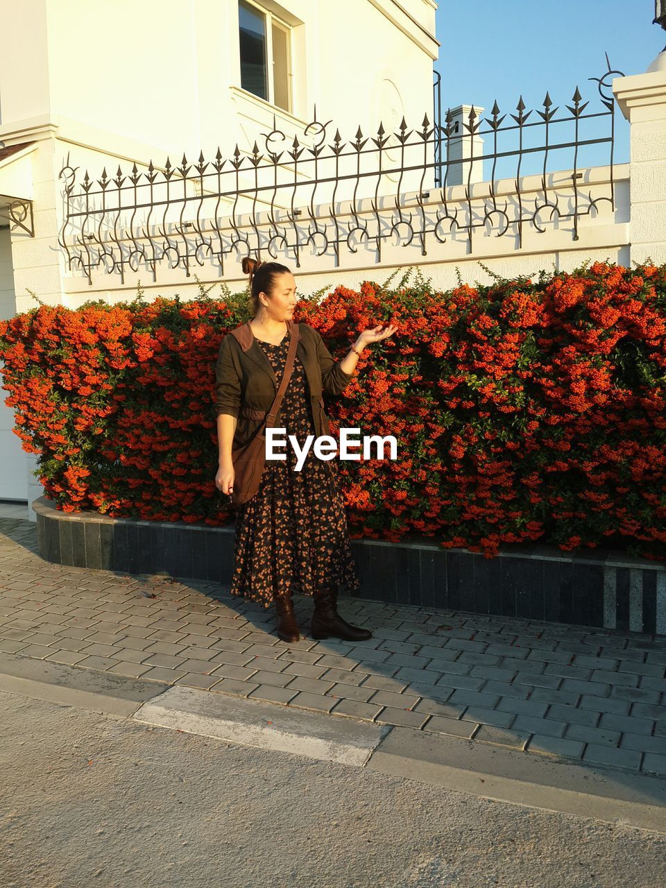 Woman standing on footpath against flowering plants 