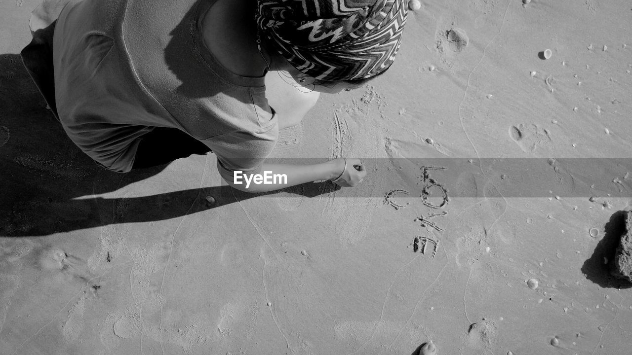 High angle view of woman writing on sand during sunny day at beach