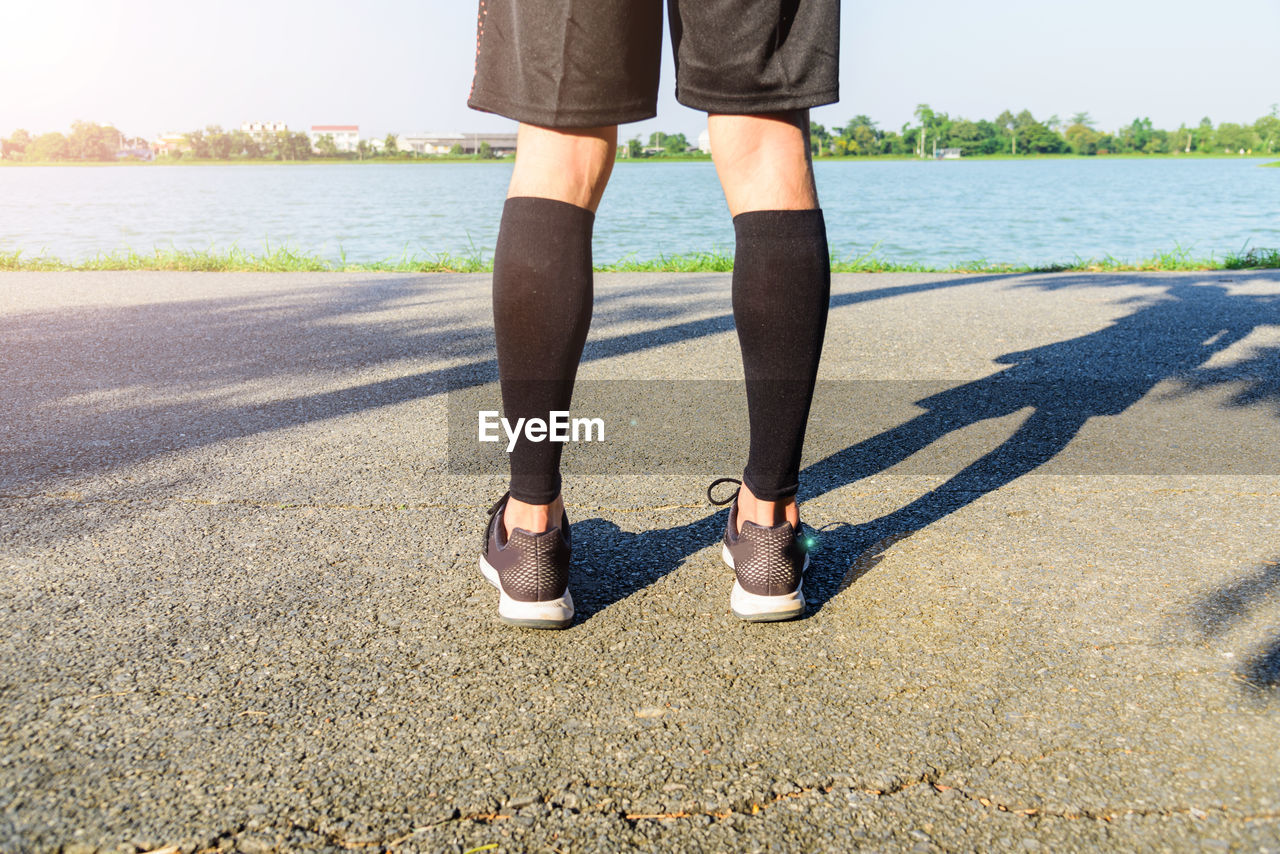 Low section of man standing on road by lake