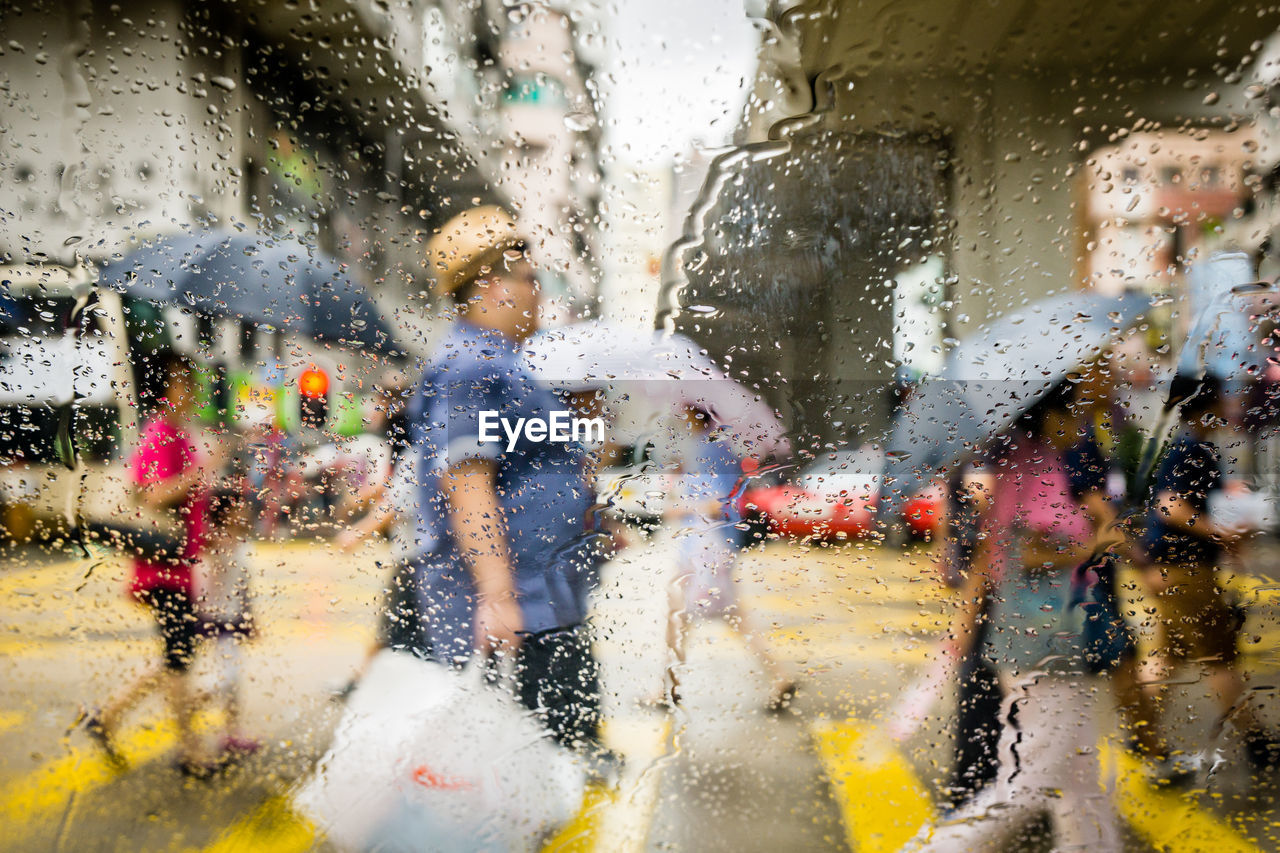 People walking on street seen through wet windshield