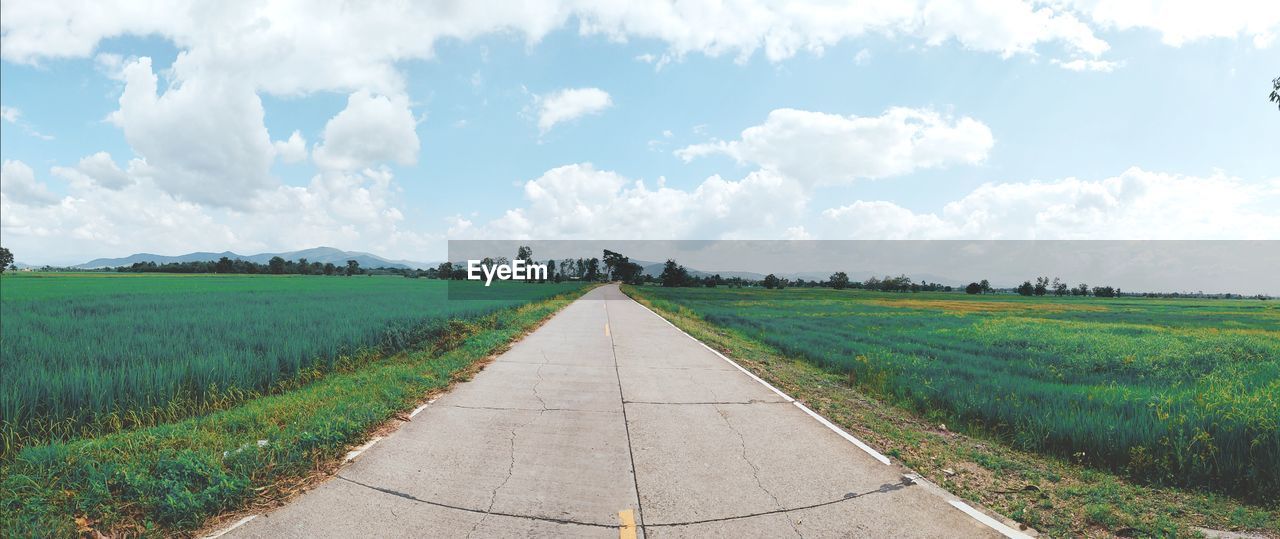 Empty road amidst field against sky