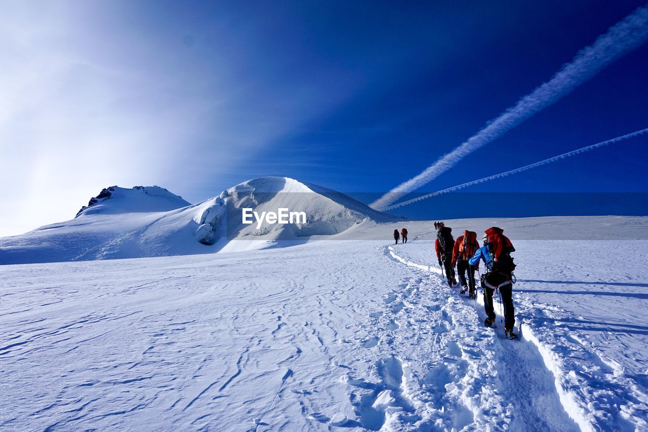 People hiking on snow covered land against sky