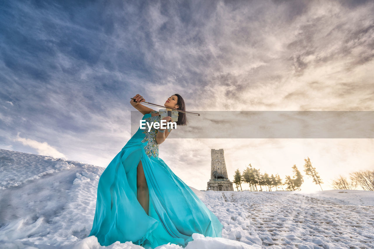 Woman playing on violin against sky during sunset