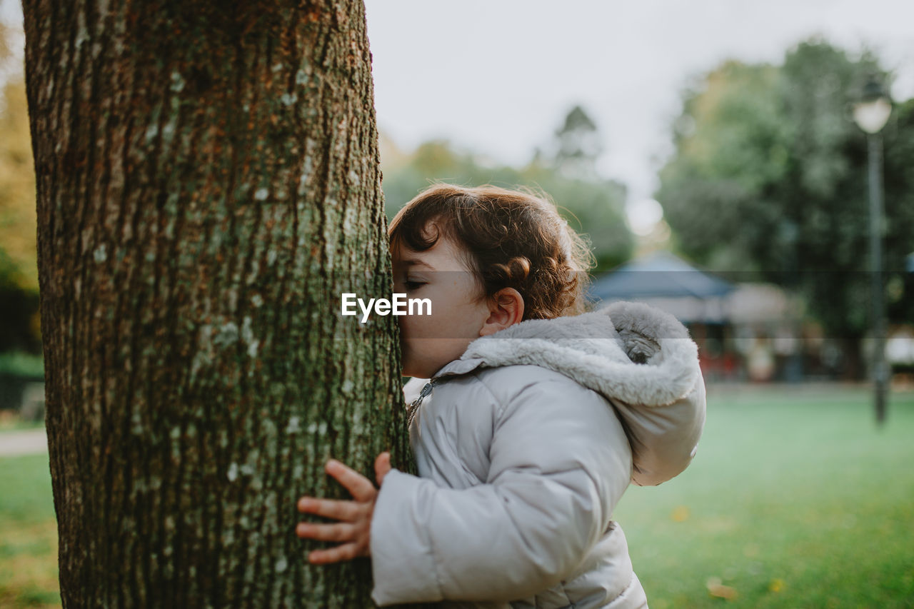 Side view of baby girl kissing tree trunk