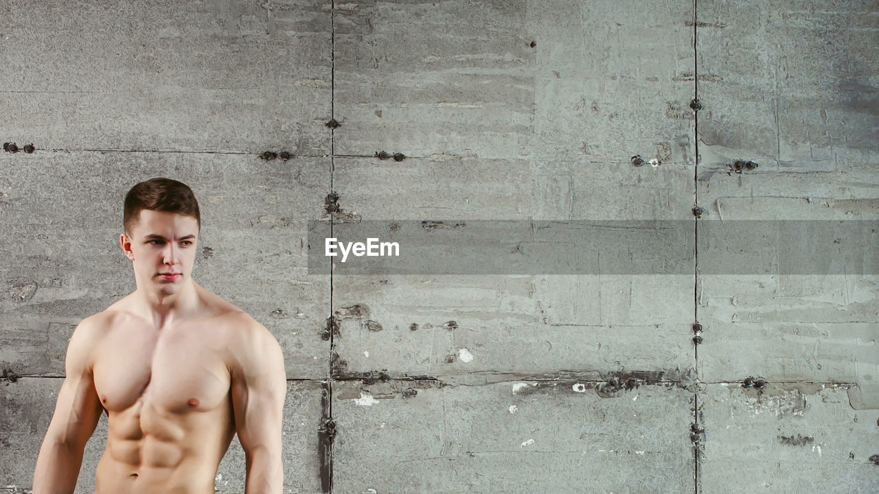 Close-up of shirtless muscular man standing by wall