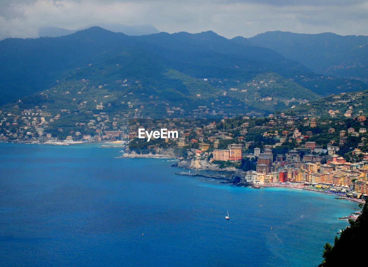 High angle view of town next to mountain against cloudy sky