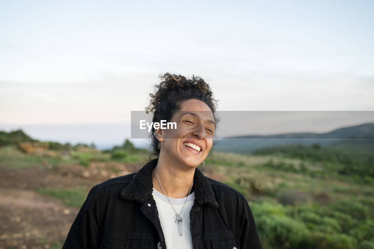 Woman smiling while standing outdoors in nature.