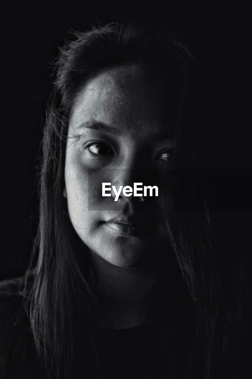 Close-up portrait of young woman against black background