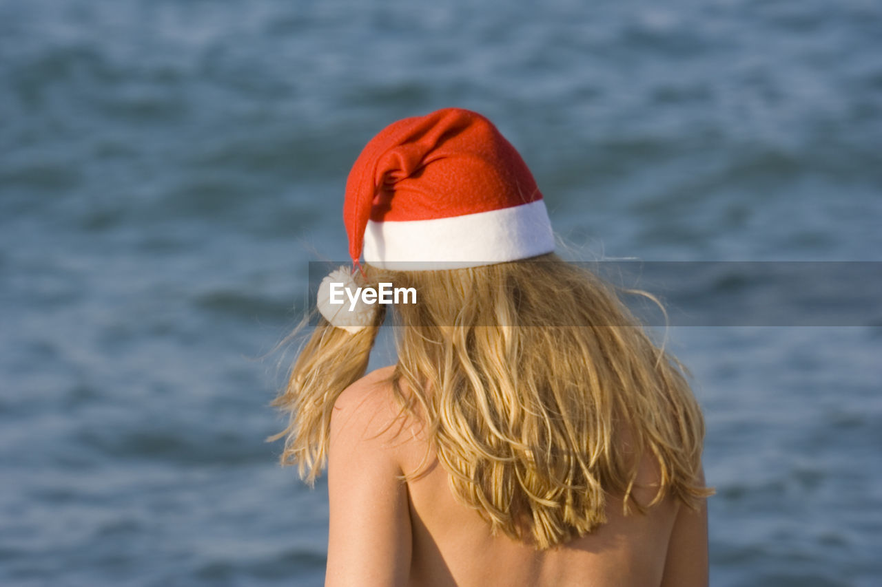 Rear view of shirtless young woman wearing santa hat against sea