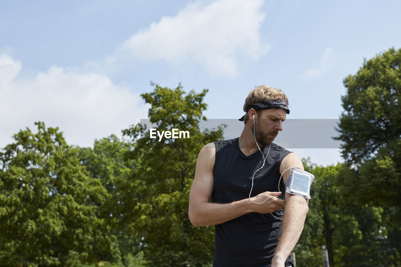 Man listening music while exercising against trees