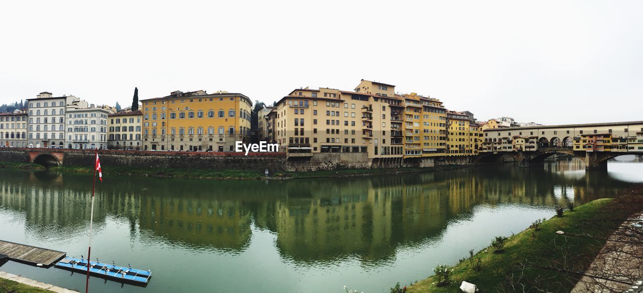 Fish-eye view of buildings by arno river canal against clear sky