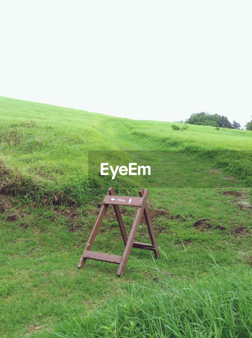 Wooden information sign on grassy hill against sky