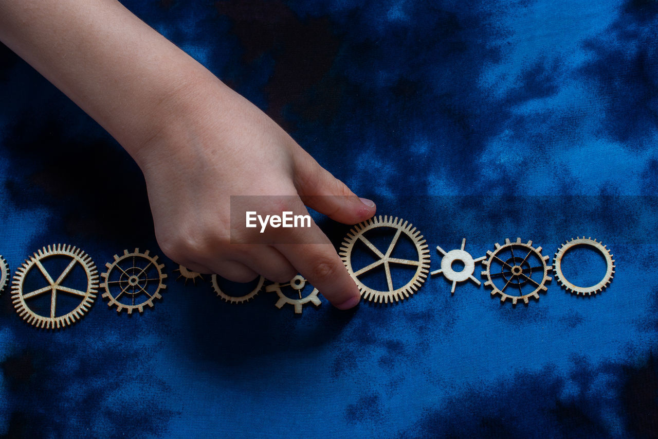 Cropped hand of person holding cogwheel over colored background