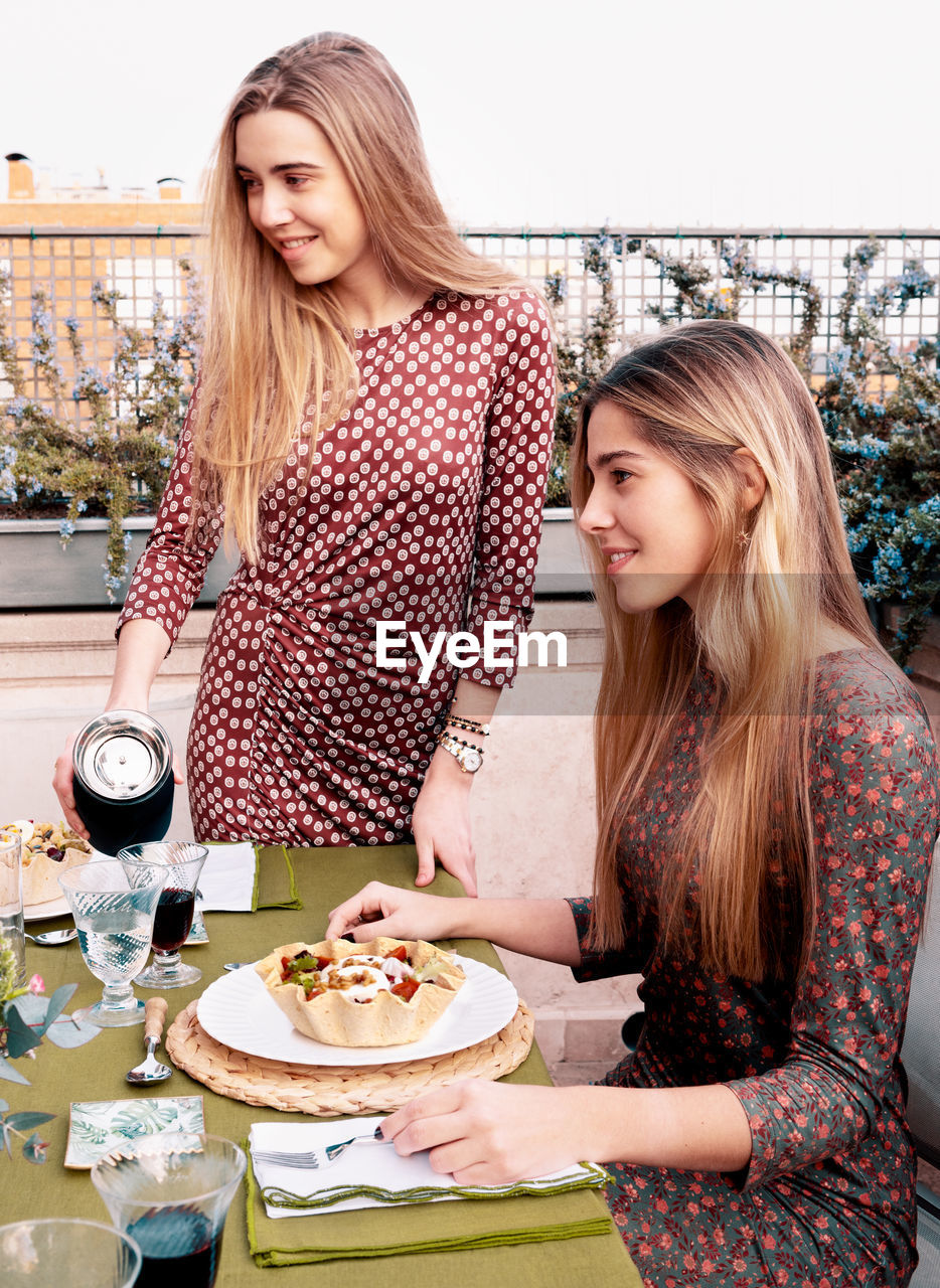 Content female friends in dresses having dinner at table with glassware and tasty salad served on terrace in summer