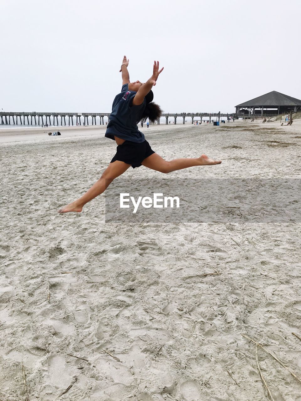 Full length side view of girl with legs apart jumping at beach