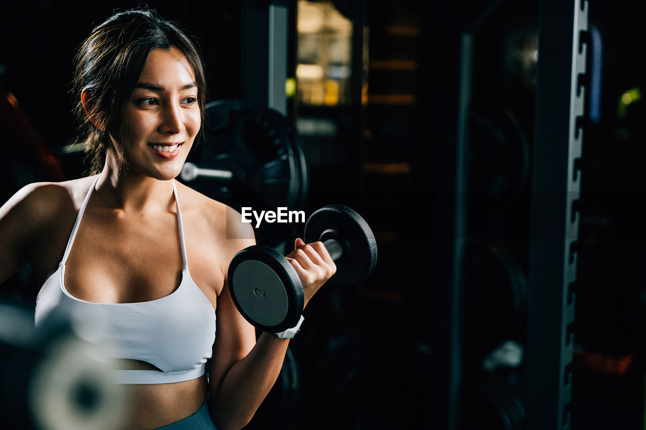 portrait of young woman lifting dumbbell in gym