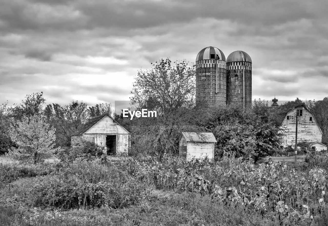 Barn and silos on field against cloudy sky