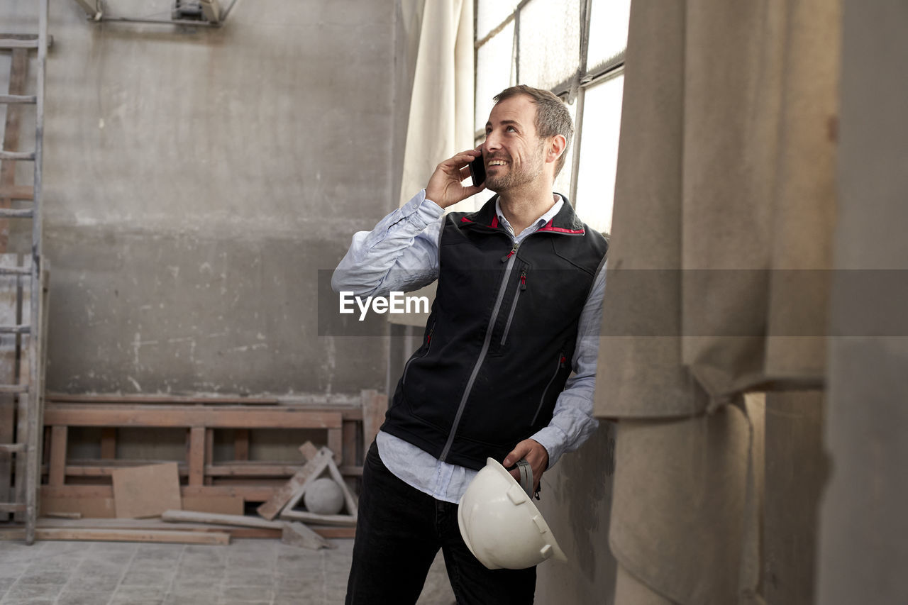 Smiling male contractor talking over smart phone while standing in building