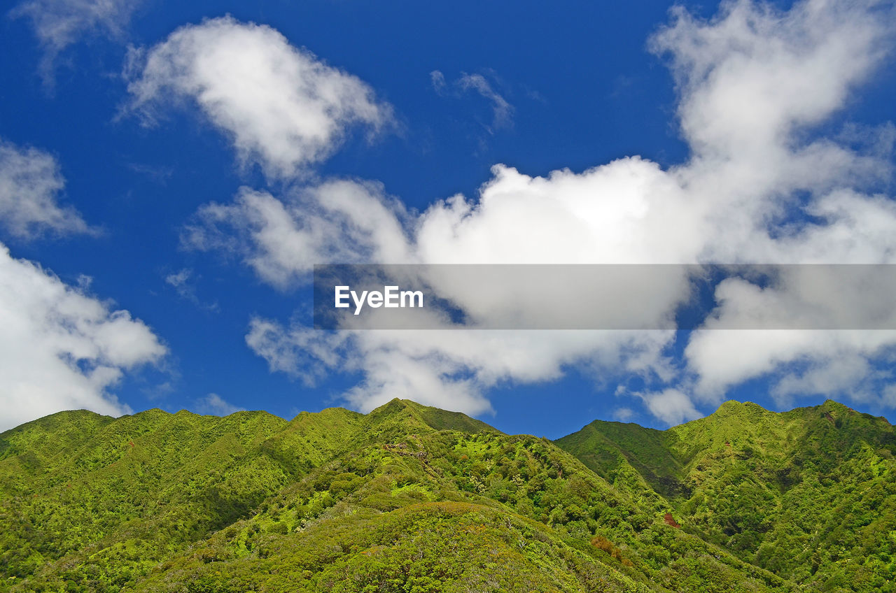 View of mountain ridge line against blue sky with clouds 