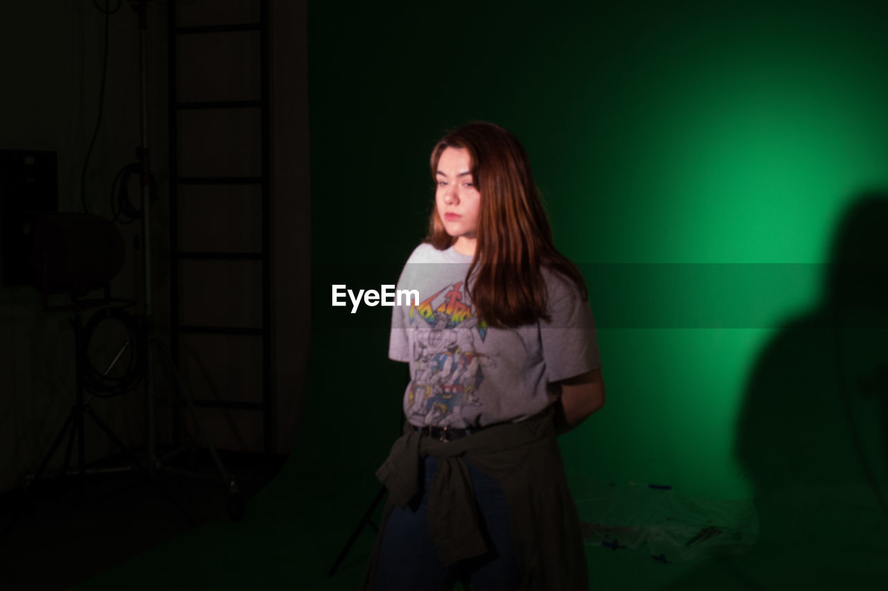 YOUNG WOMAN STANDING AGAINST WALL